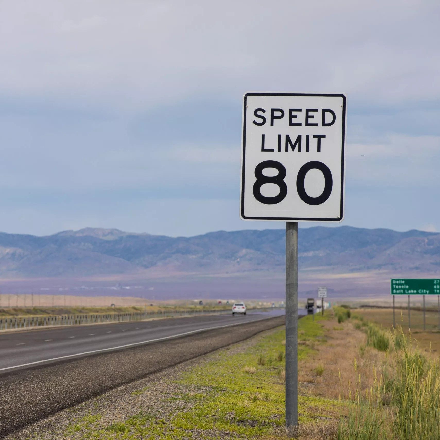 80mph speed limit sign alongside an open highway with mountains in the background
